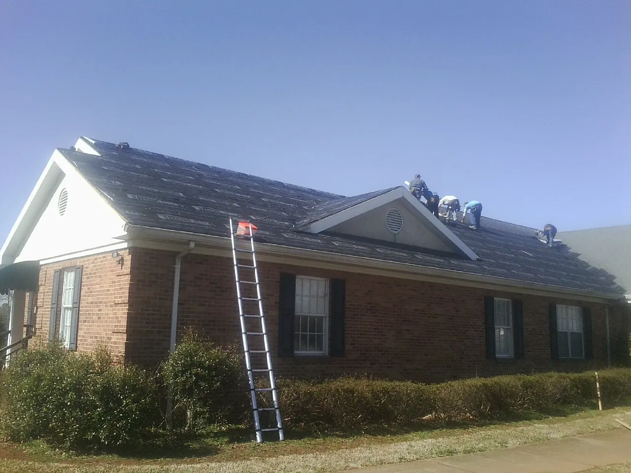 Crew tearing shingles off a brick ranch roof with a ladder set — Emergency Roof Repair work by our crew in Bowerston
