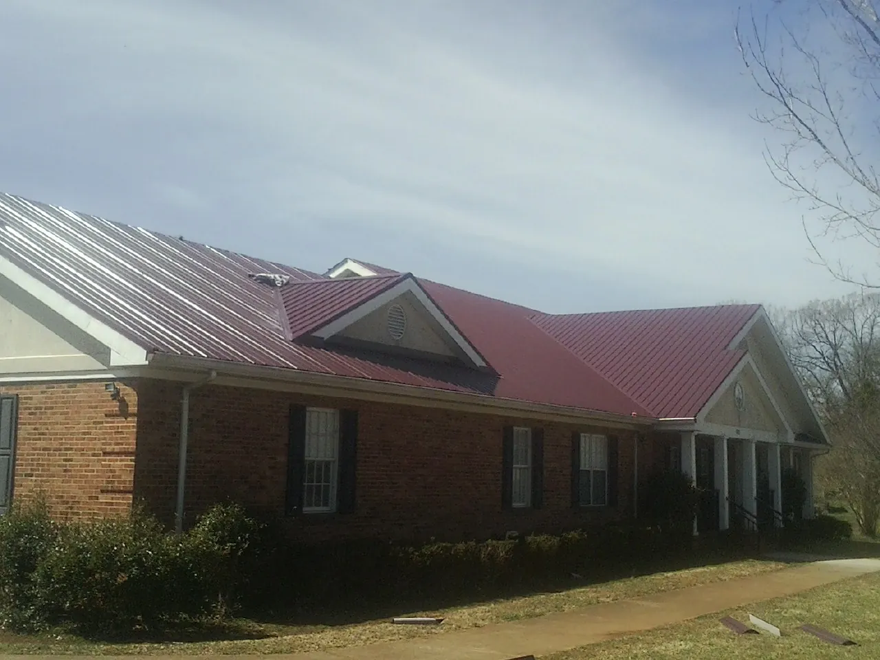 Red metal roof with gabled entries on a long brick building, from a Hail Damage Roof Repair job in Bowerston