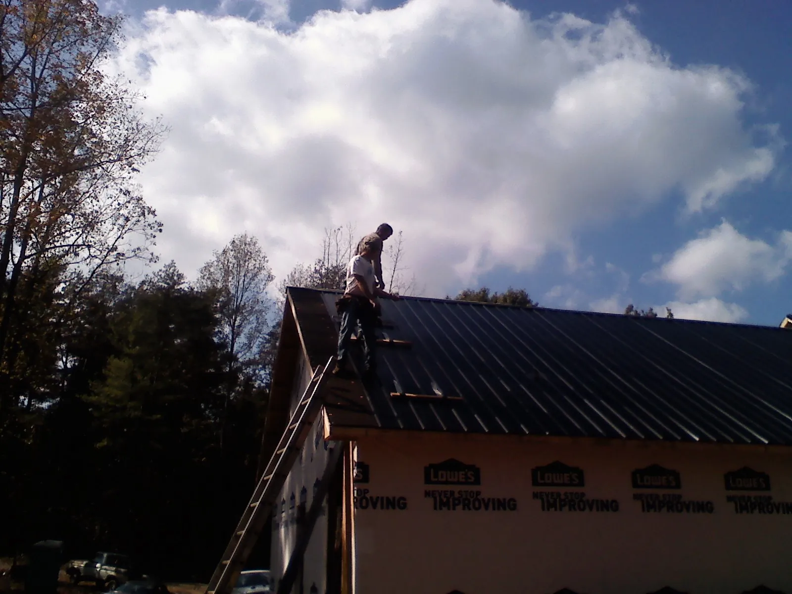 Roofer fastening dark metal panels high against a cloudy sky, from a Roof Inspection job in Bowerston
